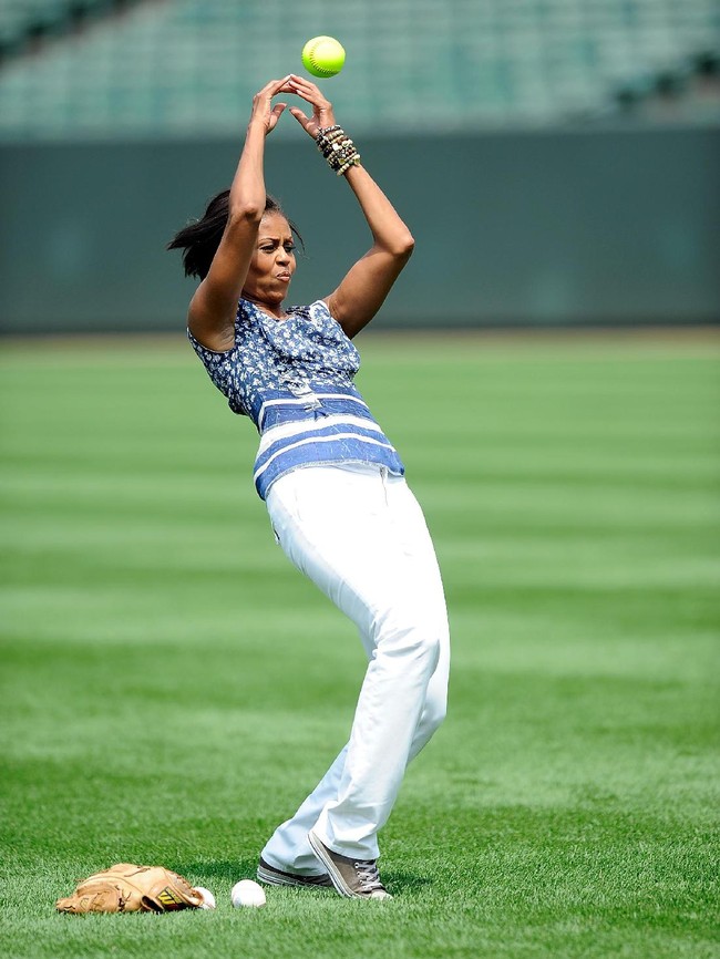 Michelle Obama saat bermain softball di Baltimore, AS, 2010, silam. Baju bernuansa biru dengan permainan motif, jeans putih, dan sneakers Converse jadi andalannya. (Foto: Getty Images)