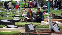 Dua orang peziarah membaca ayat-ayat suci Alquran di depan makam keluarga.