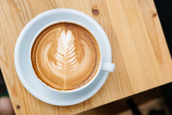 Cup of coffee with macaron on white wooden table from above, flat lay