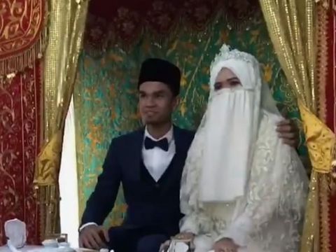 Muzammil dan istri nampak malu-malu saat duduk di pelaminan.