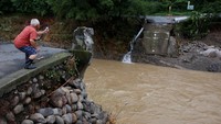 Seorang warga tengah mengabadikan sebuah jembatan yang hilang pasca diterjang banjir. REUTERS/Issei Kato.