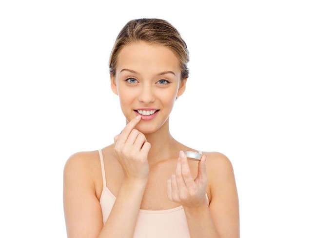 beauty, people and lip care concept - smiling young woman applying lip balm to her lips