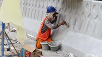 Pekerja tengah mengecat pembatas jalan.