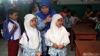 Seorang guru menunjukkan bangku untuk para muridnya.