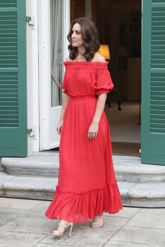 Kate tampil dengan gaya berbeda memakai gaun maxi off the shoulder keluaran rumah mode Alexander McQueen. Gaun merah yang memikat dipadukan bersama sepatu hak tinggi warna nude dari Prada.