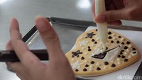 Cara melukis kue pun sangat mudah. Traveler tinggal memencet isi wadah kue cokelat dan keju di atas kue (Baban/detikTravel)