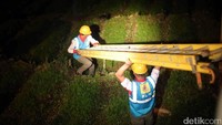 Dua orang petugas PLN menggotong tangga di tengah kegelapan.