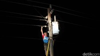 Petugas mengecek trafo dengan penerangan lampu senter.