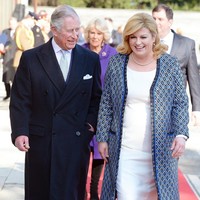 Untuk menyambut Pangeran Charles dan istrinya Camilla, Kolinda Grabar-Kitavoric memilih padanan gaun pas badan warna putih yang dipadukan mantel bermotif geometris. Gaya yang elegan sekaligus anggun. Foto: Getty Images