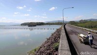 Seorang warga mendorong gerobak di jalan sekitar waduk.
