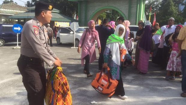 Personel polisi membantu mengangkat tas milik calon jemaah haji.