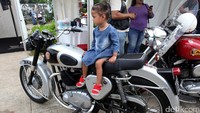 Seorang anak tampak asyik duduk di atas motor yang dipamerkan.