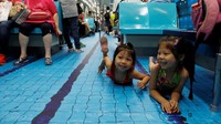 Tetapi itu bukanlah kolam sungguhan, lantai MRT tersebut didekorasi sedemikian rupa menyerupai kolam renang. Lucunya mereka tampil lengkap dengan kacamata dan baju renang. REUTERS/Tyrone Siu.