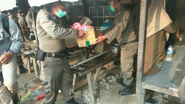 Petugas Satpol PP membantu membawa barang-barang milik warga di Taman BMW.