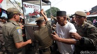 Seorang pedagang berusaha mengamankan gerobaknya yang diangkut petugas.