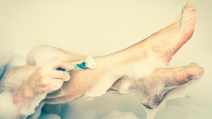 645034972 Woman shaving legs with razor in bathroom at home