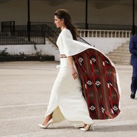 Gaun putih minimalis datang dengan ornamen lengan cape dramatis dan memiliki kejutan motif di baliknya. Foto: Dok. Instagram/Queen Rania Al Abdullah