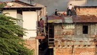 Angin kencang, asap ke mana-mana. Karena lokasi kebakaran berada di gang sempit, petugas pemadam kebakaran melewati atap-atap rumah itu untuk mencapai titik pemadaman. / Foto: Muhammad Fida Ul Haq/detikcom