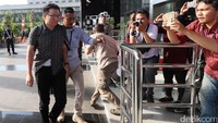 Dia tampak mengenakan kemeja bermotif dan dituntun masuk oleh petugas KPK.