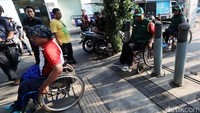 Seorang warga mengecek lebar tiang penghalang di jalur pedestrian dengan kursi roda.