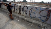 Seorang anak bermain di pinggir Kali Ciliwung yang penuh coretan.