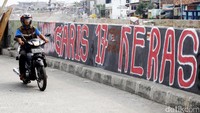 Pemotor melintas di samping coretan dinding kegelisahan warga.