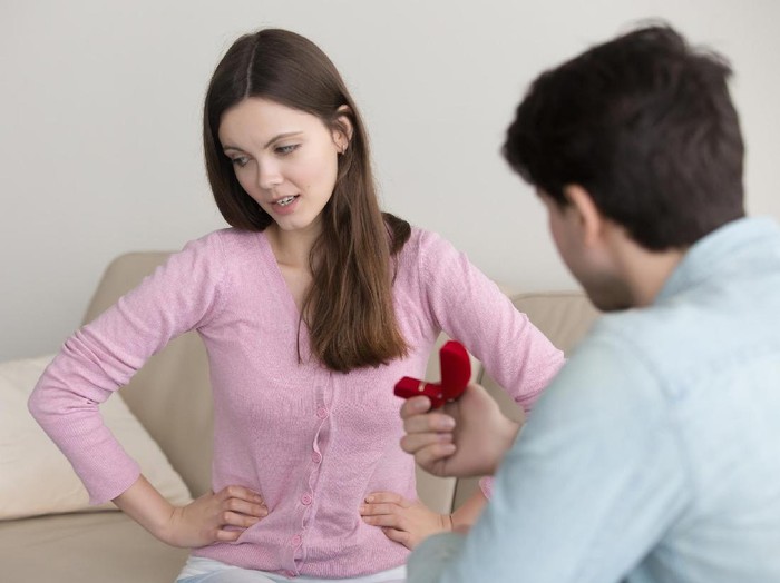 Young man proposing to girlfriend, asking to marry, engagement ring box. Lady hesitating, having doubt, reluctant, thinking of refusal. Unpleasant surprise, bad birthday gift, disappointment in love