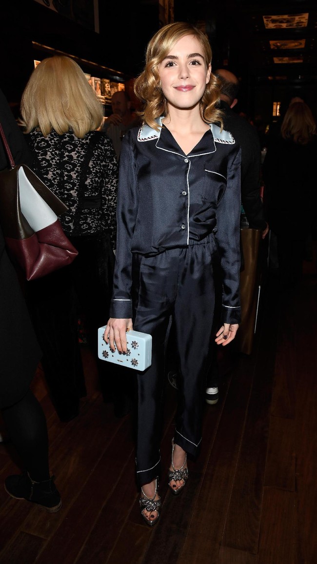 Aktris muda Kiernan Shipka membungkus tubuhnya dengan piama satin berwarna midnight blue. Melengkapi gayanya, clutch boxy dan sandal heels. Foto: Getty Images