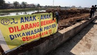 Spanduk larangan bermain di area proyek terpampang di tanggul sungai.