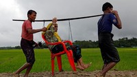 Dua orang warga yang memikul seorang nenek melintasi persawahan yang licin. Mohammad Ponir Hossain/Reuters.