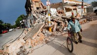 Seorang pria berdiri dengan sebuah sepeda di dekat sebuah bangunan yang hancur di Juchitan. (REUTERS/Edgard Garrido)