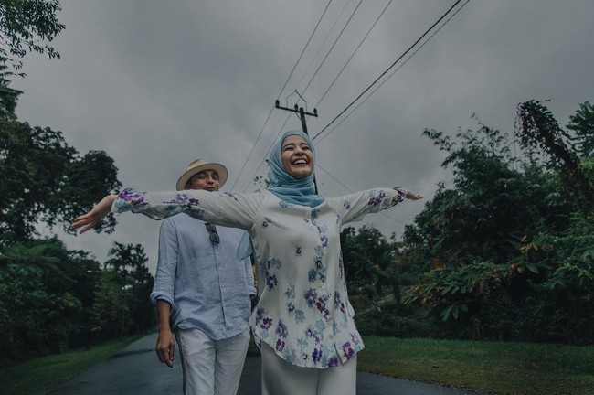 Keceriaan Laudya Cynthia Bella terlihat di foto prewedding outdoor ini. Ia tertawa bahagia sambil merentangkan tangannya ketika berjalan membelakangi Engku Emran. Konsep baju putih-biru muda membuat penampilan mereka terlihat serasi. Foto: Dok. Instagram @alvasus