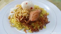 Seporsi nasi kuning berisi nasi kuning, dengan topping kering kentang pedas, mie, ikan tongkol, serta telur rebus. Sebagai pelengkapnya ada acar dan juga sambal pedas (Wahyu/detikTravel)