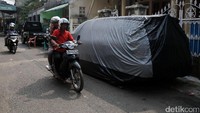 Pengendara sepeda motor melintas di samping mobil yang diparkir di bahu jalan di kawasan Bukit Duri, Jakarta Selatan.