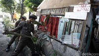 Dua orang petugas berusaha merobohkan bangunan menggunakan kayu.