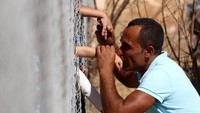 Sambil berlutut, Ammar Hammasho mencium satu persatu anak laki-lakinya dengan dibatasi pagar setinggi 3 meter. (Foto: REUTERS/Yiannis Kourtoglou)