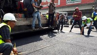 Petugas mengukur lebar jalan yang diaspal.