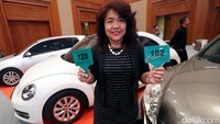 Seorang warga menunjukkan tanda peserta di depan mobil yang dilelang.