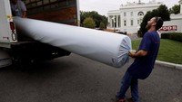 Seorang pekerja tampak mengeluarkan karpet baru yang akan dipasang di Gedung Putih. Furnitur, karpet, dan dekorasi yang ada di Ruang Oval Gedung Putih beberapa akan diganti (Jim Bourg/Reuters)