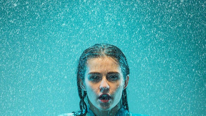 The portrait of young beautiful woman in the rain. The girl standing on a turquoise background