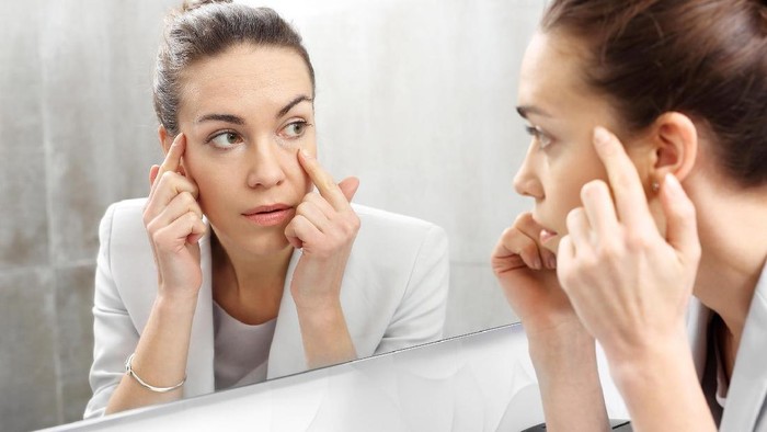 Reflection in the mirror. Woman looks in the mirror noticing the first wrinkles