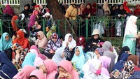 Massa berkumpul dengan duduk-duduk di depan gedung DPR. Sebagian dari mereka bersandar di pagar gedung.