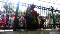 Seorang ibu keluar dengan menyelip di antara pagar besi.