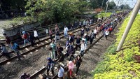 Para penumpang berjalan menyelusuri rek kereta api.