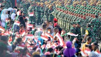 Warga mengibarkan bendera Merah Putih saat defile pasukan TNI melintas.