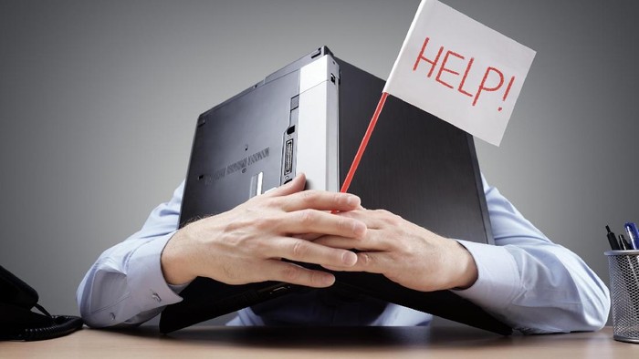 Frustrated and overworked businessman burying his head uner a laptop computer asking for help