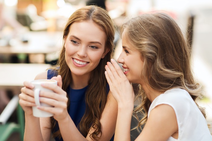 501541470 people communication and friendship concept - smiling young women drinking coffee or tea and gossiping at outdoor cafe
