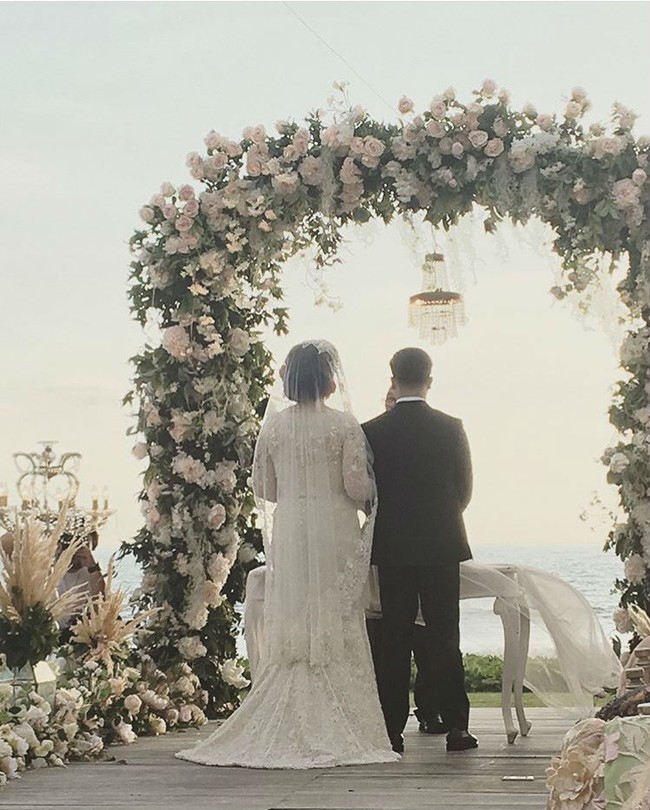 Pernikahan Derby dan Claudia diresmikan di depan arch tertutup bunga berlatar belakang laut. Foto: Dok. Instagram