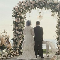 Pernikahan Derby dan Claudia diresmikan di depan arch tertutup bunga berlatar belakang laut. Foto: Dok. Instagram