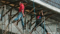 Tiga pekerja sedang menurunkan kayu penyangga.